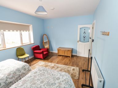 A bedroom with two floral beds a red armchair a green chair a wooden chest and a mirror at The Water's Edge in Boyle County Roscommon