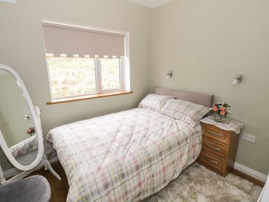 A bedroom with a double bed a window a wooden nightstand with flowers and a standing mirror at The Water's Edge in Boyle County Roscommon