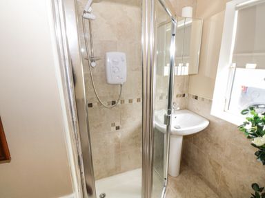 A bathroom with a shower enclosure a pedestal sink and a window with a roller blind at The Water's Edge in Boyle County Roscommon