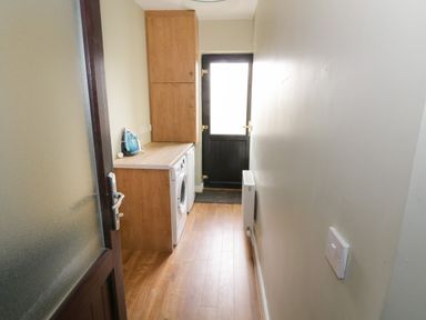 A narrow utility room with wooden cabinets a washing machine an iron on the countertop and a black door at the end at The Waters Edge in Boyle County Roscommon