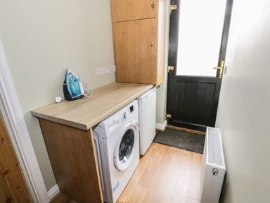 A utility room with a washing machine an iron a small fridge wooden cabinets and a black door at The Water's Edge in Boyle County Roscommon