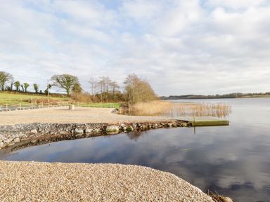 A lakeside area with a pebble beach and a wooden dock surrounded by reed beds at The Water's Edge in Boyle County Roscommon