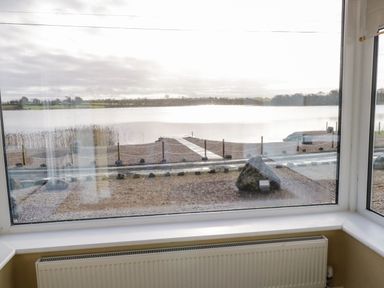 A window view overlooking a lake with a pier and a gravel pathway at The Waters Edge in Boyle County Roscommon