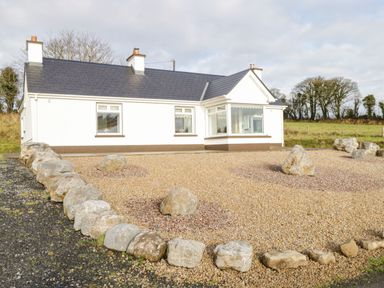 A single-story house with white walls and a dark roof surrounded by a rock-bordered gravel yard at The Water's Edge in Boyle County Roscommon