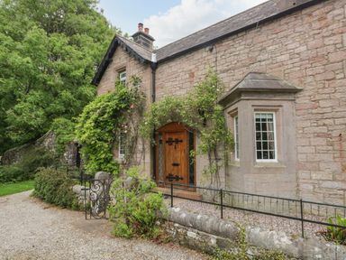 The exterior of a stone house with a wooden door and climbing plants at The Lodge in Greystoke
