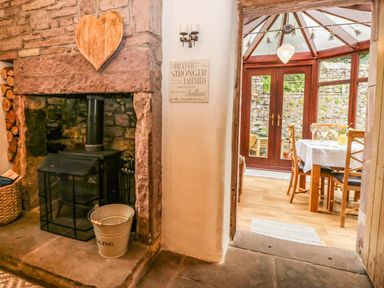 A wood burning stove set in a stone fireplace next to a dining area with a table and chairs at The Lodge in Greystoke