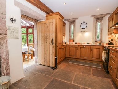 A kitchen with wooden cabinets clock on wall and a wooden door leading to a dining area at The Lodge in Greystoke