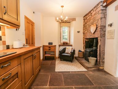 A room with wooden cabinets a black armchair near a fireplace and a small wooden table at The Lodge in Greystoke