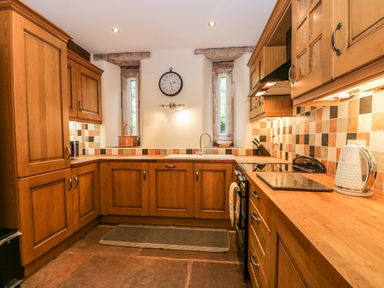 A kitchen with wooden cabinets tiled backsplash and clock on the wall at The Lodge in Greystoke