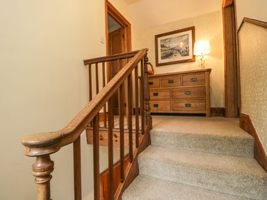 A stairway with carpeted steps wooden railing and a wooden dresser with a lamp and picture on the wall at The Lodge in Greystoke