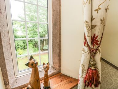 A window with two wooden cat figurines on the windowsill and a curtain with a tieback at The Lodge in Greystoke