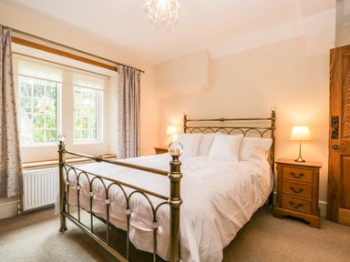 A bedroom with a metal bed frame, white bedding, bedside tables with lamps, and a window with floral curtains at The Lodge in Greystoke