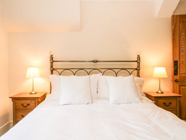 A bedroom with a bed with brass headboard two white pillows two bedside tables with lamps and a wooden door at The Lodge in Greystoke
