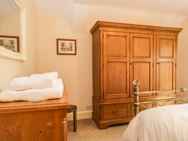 A bedroom with a wooden wardrobe a chest of drawers with towels a metal bed frame and a framed picture on the wall at The Lodge in Greystoke