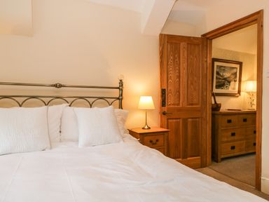 A bedroom with a metal bed frame bedside table and lamp visible through an open wooden door at The Lodge in Greystoke