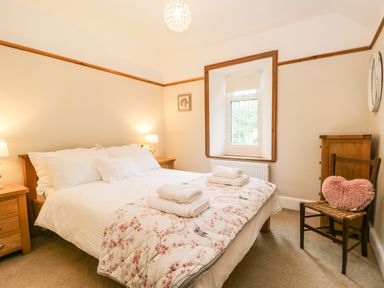 A bedroom with a double bed white bedding floral blanket wooden furniture and a window at The Lodge in Greystoke