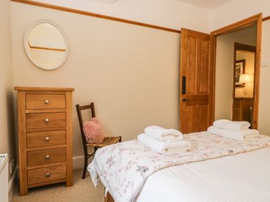 A bedroom with a wooden dresser a chair with a pink cushion a bed with folded towels and an open wooden door at The Lodge in Greystoke