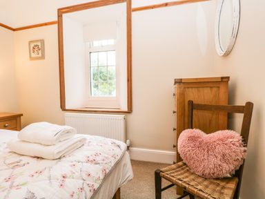 A bedroom with a bed with folded towels a wooden chair with a pink heart pillow a wooden chest of drawers and a window at The Lodge in Greystoke