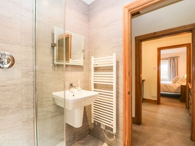 A bathroom with a sink mirror towel heater and a view into a bedroom at The Lodge in Greystoke