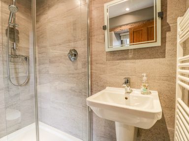 A bathroom with a shower enclosure a white sink with a faucet and a mirror on the wall at The Lodge in Greystoke