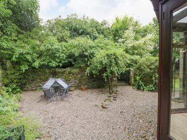 A gravel garden patio with overturned chairs and a table near stone walls and greenery at The Lodge in Greystoke