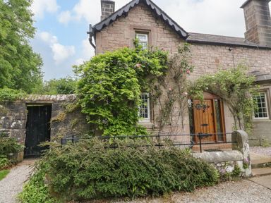 A stone cottage with wooden door and windows surrounded by climbing plants and bushes at The Lodge in Greystoke