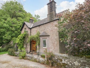 A stone house with a wooden door surrounded by plants and trees at The Lodge in Greystoke