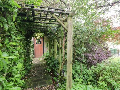 A wooden pergola with greenery around it leading to a wooden door at The Lodge in Greystoke