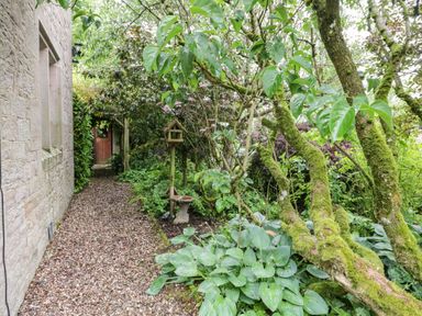 A gravel path along a stone wall with green plants and a bird feeder at The Lodge in Greystoke