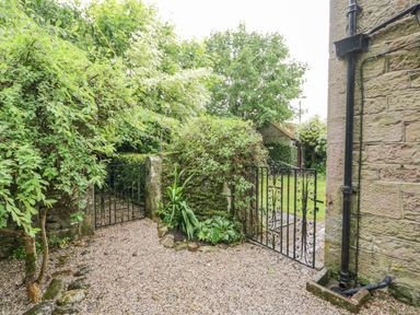 A gravel area with metal gates and stone walls surrounded by trees and plants at The Lodge in Greystoke