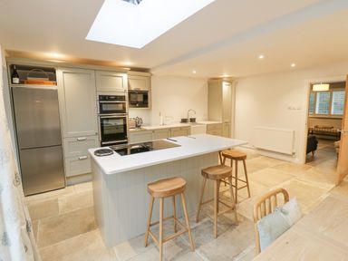 A kitchen with an island and three wooden stools at Dazie Cottage in Broadway