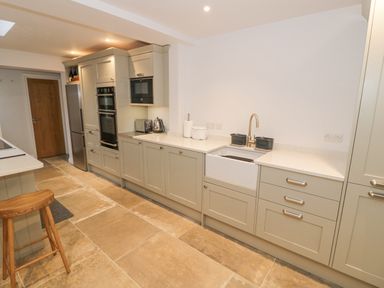 A kitchen with beige cabinets a white countertop sink and wooden stool at Dazie Cottage in Broadway