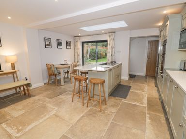 A kitchen with a central island and stools a small dining table with chairs and sliding glass doors at Dazie Cottage in Broadway