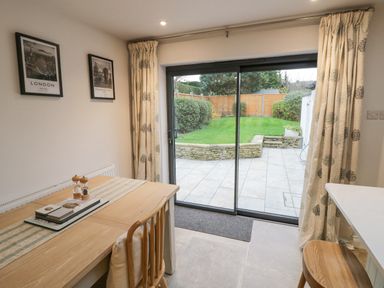 A dining area with a wooden table and chairs next to sliding glass doors leading to a garden at Dazie Cottage in Broadway