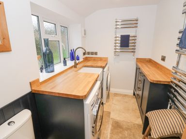 A utility room with a washing machine dryer wooden countertops and towel racks at Dazie Cottage in Broadway