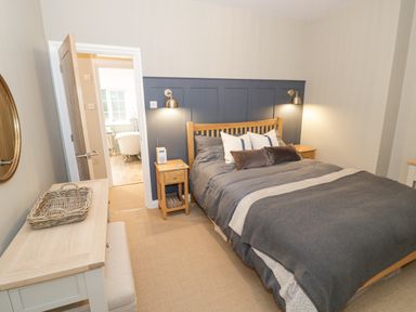 A bedroom with a wooden bed and bedside tables and an open door leading to a bathroom at Dazie Cottage in Broadway