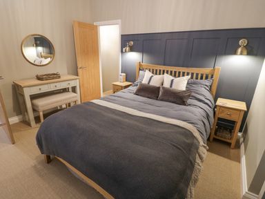 A bedroom with a wooden bed and nightstands two wall lamps and a desk with a round mirror in Dazie Cottage Broadway