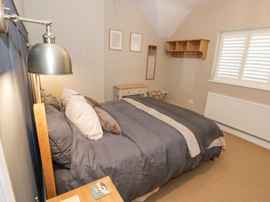 A bedroom with a double bed grey bedding wooden side table and wall-mounted lamp at Dazie Cottage in Broadway