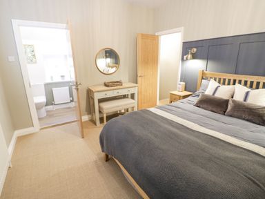 A bedroom with a bed a bedside table a dressing table and an open door to a bathroom at Dazie Cottage in Broadway