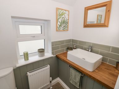 A bathroom with a white sink on a wooden countertop a window and a mirror at Dazie Cottage in Broadway