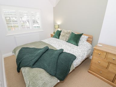 A bedroom with a bed dressed in green and white bedding with green pillows and a wooden chest of drawers at Dazie Cottage in Broadway