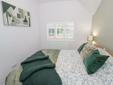 A bedroom with a bed covered in patterned bedding and green pillows a bedside lamp and a geometric wall art at Dazie Cottage in Broadway