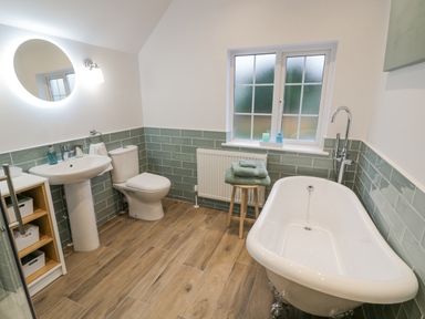 A bathroom with a pedestal sink toilet freestanding bathtub wooden stool with folded towels and a window at Dazie Cottage in Broadway