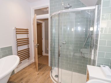 A bathroom with a glass enclosed shower a wooden towel rail a sink and a wooden door at Dazie Cottage in Broadway
