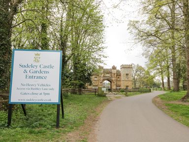 A road leading to a stone gatehouse with an arch and a large sign for Sudeley Castle and Gardens entrance