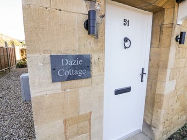 A white door with number 51 and a sign reading Dazie Cottage on a stone wall at Dazie Cottage in Broadway
