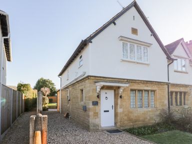 A two-story house with a stone lower facade and white upper facade with a gravel driveway at Dazie Cottage in Broadway