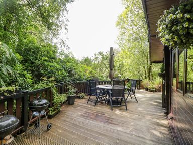 An outdoor wooden deck with a table and chairs surrounded by green trees at Scafell Lodge Skiptory Howe 7 White Cross Bay Holiday Park near Windermere