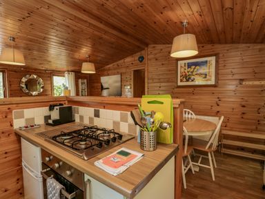 A kitchen with a gas stove oven and utensils next to a dining area with a round table and chairs at Scafell Lodge Skiptory Howe 7 White Cross Bay Holiday Park near Windermere