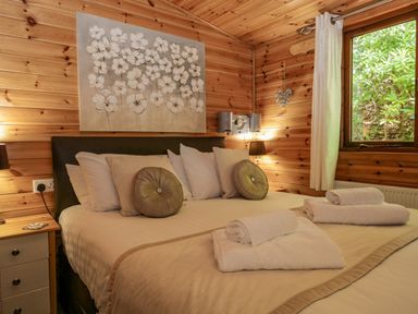 A bedroom with a bed with multiple pillows and folded towels on it inside a wooden cabin at Scafell Lodge Skiptory Howe 7 White Cross Bay Holiday Park near Windermere